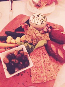 Cheese board with pickled veggies, marinated olives, goat cheese, pretzel rolls and edamame hummus